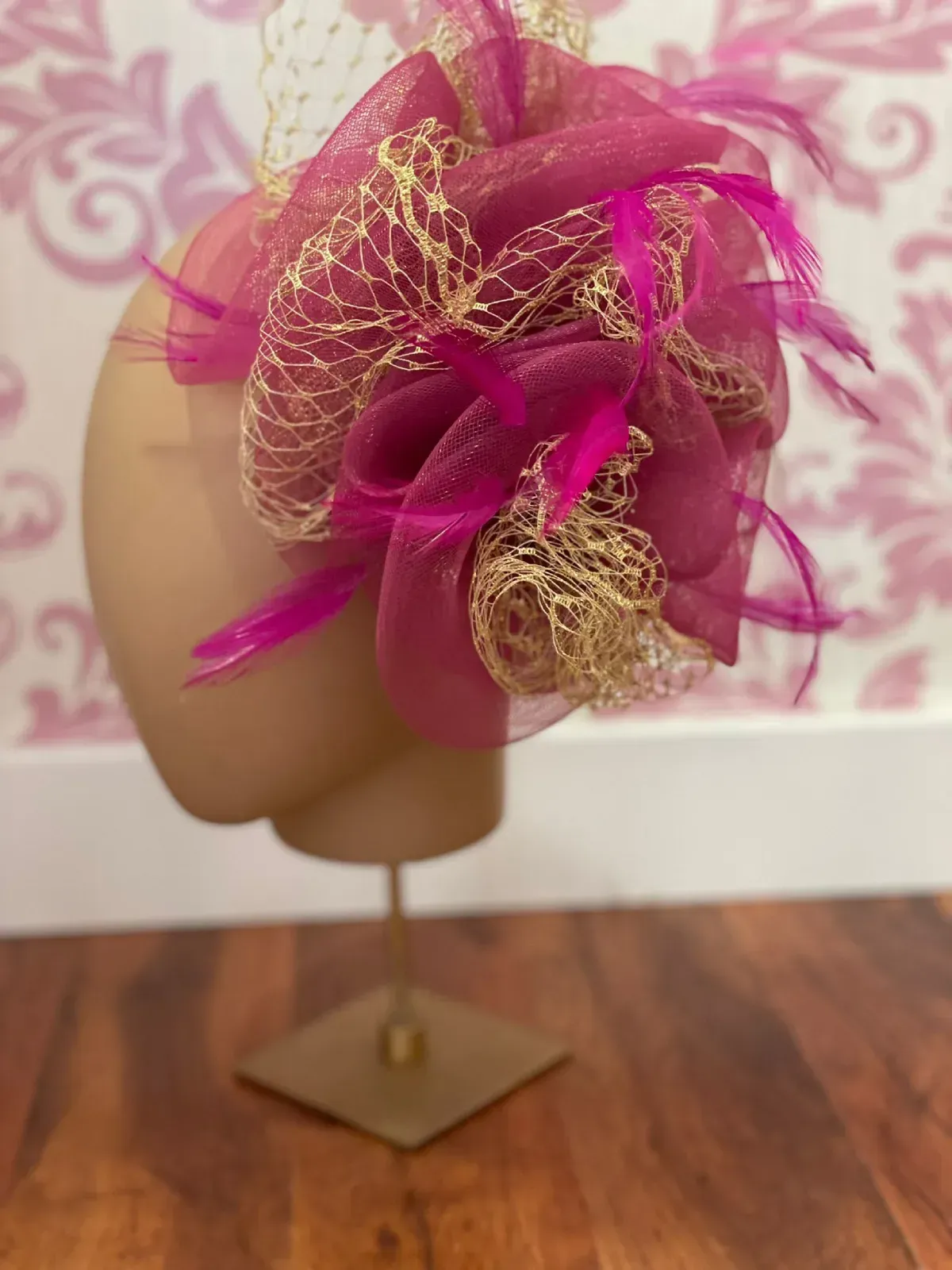 Tocado rosa con red dorada y plumas sobre cabeza de maniquí.