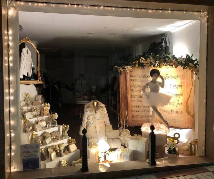 Un escaparate con un maniquí de bailarina, partituras y regalos en tonos dorados.