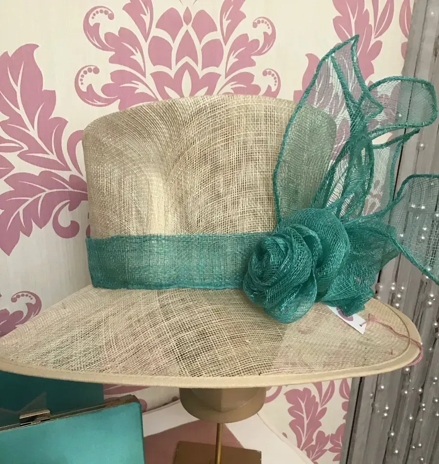 Sombrero color canela y turquesa con detalles florales sobre un fondo rosa estampado.