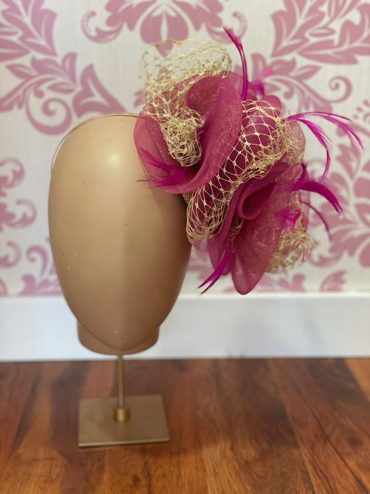 Un tocado con detalles en rosa y dorado sobre una cabeza de maniquí, sobre un fondo de pantalla floral.