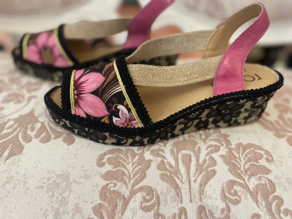 Sandalias florales rosas con ribete negro y una tira rosa sobre una superficie estampada.