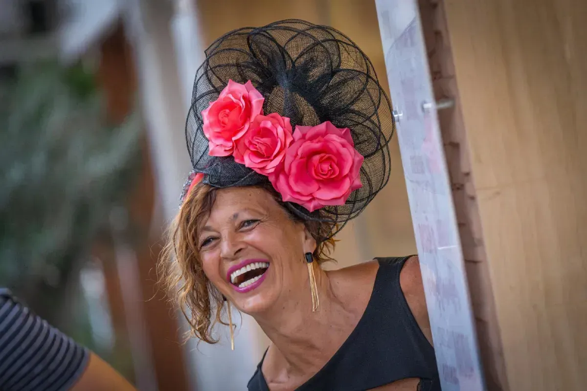 Mujer con sombrero negro con rosas rosadas, riendo; al aire libre.