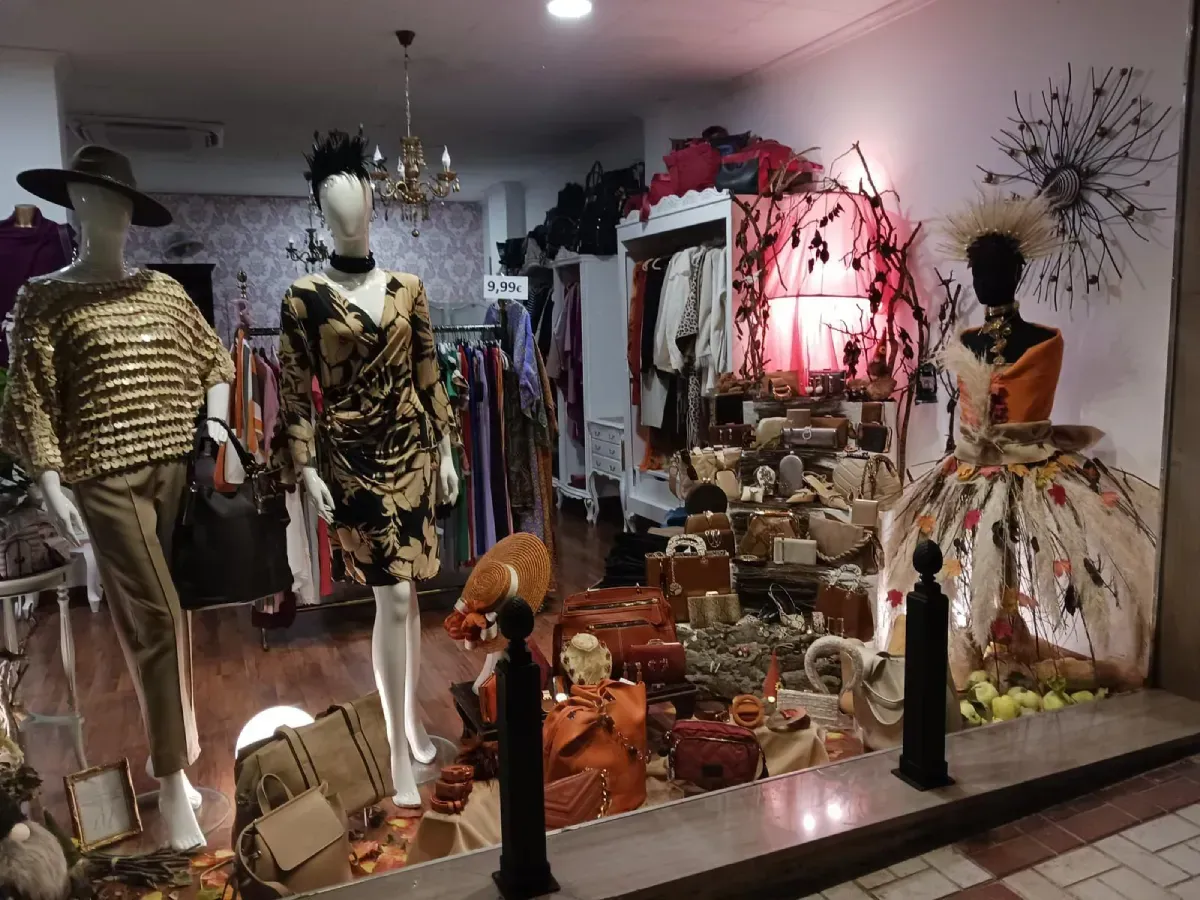 Escaparate de una boutique, con maniquíes con trajes de moda, accesorios y ropa en percheros. Iluminación cálida.