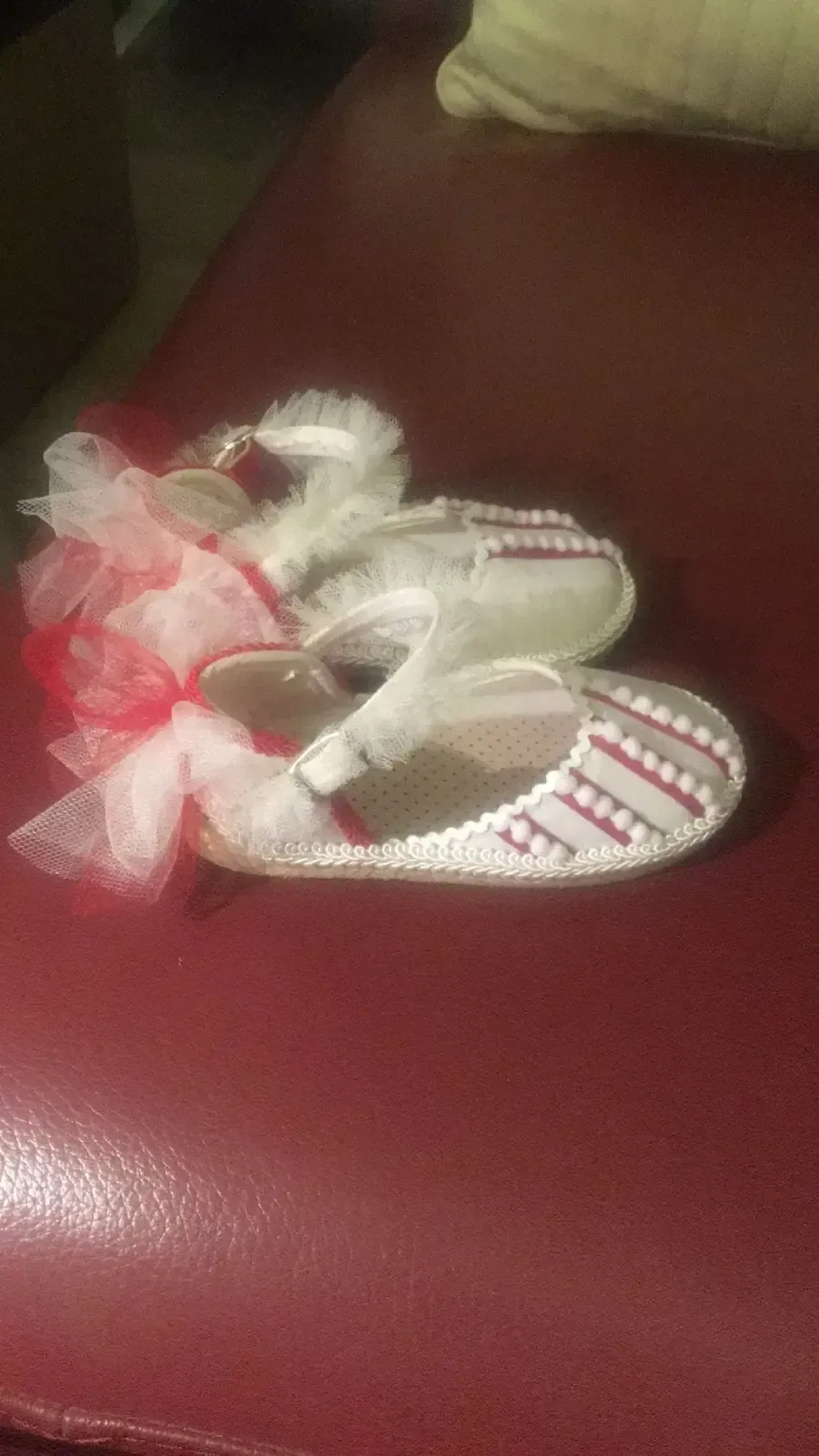 Zapatitos de bebé con detalles en blanco y rojo, lazos de tul, sobre superficie granate.