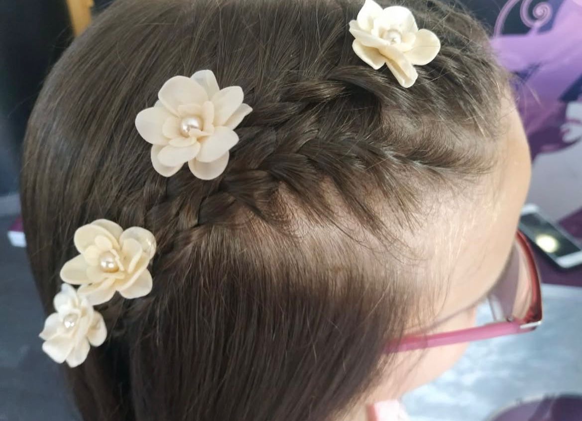 Primer plano de cabello castaño peinado con una trenza y adornado con pinzas para el cabello con flores de color beige.