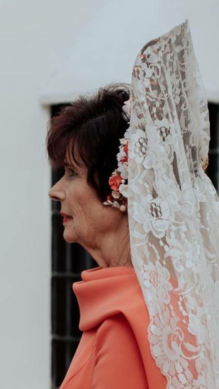 Mujer con vestido color coral y velo mantilla de encaje, perfil lateral.