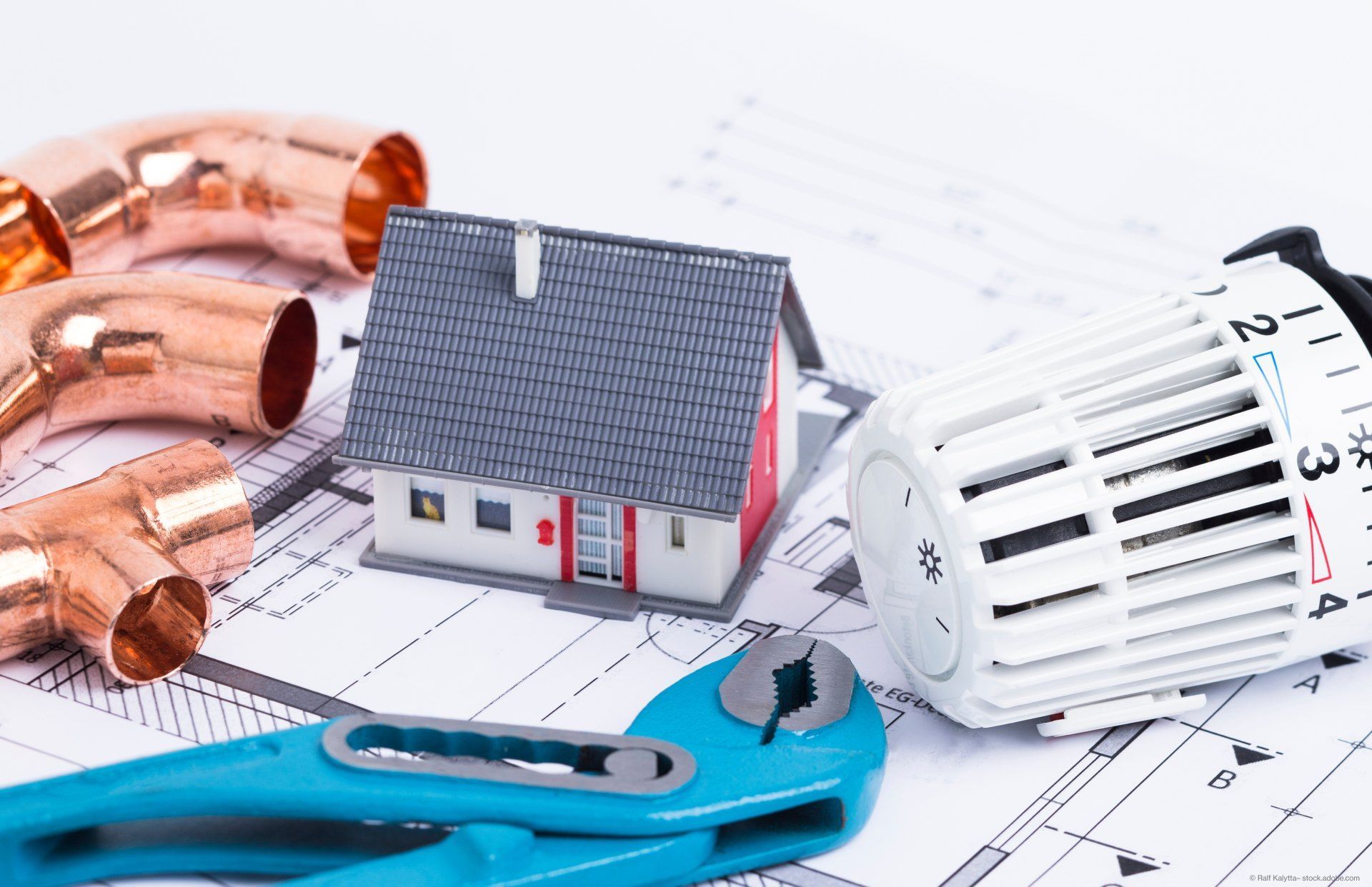 Modellhaus, Heizungsrohre, Zange und Heizungsrad auf einem Bauplan