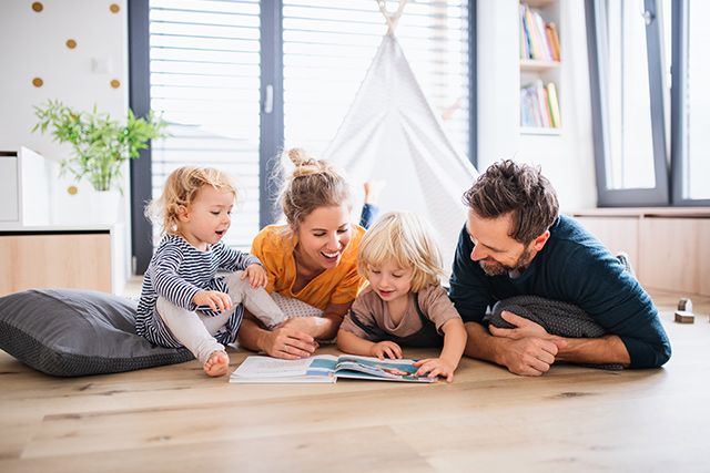 Famille souriante réunie sur le sol autour d’un livre pour enfant