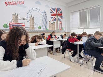 Estudiantes realizando un examen en un aula luminosa con murales en inglés y decoración mural con temática británica.