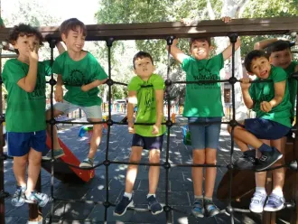 Grupo de niños con camisetas de color verde brillante posando en unas escaleras bajo una glorieta de mosaico al aire libre.