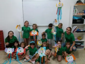 Niños con camisetas verdes posando con coloridas manualidades de papel en un aula.