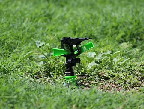 Un aspersor verde y negro se encuentra sobre un exuberante césped verde.