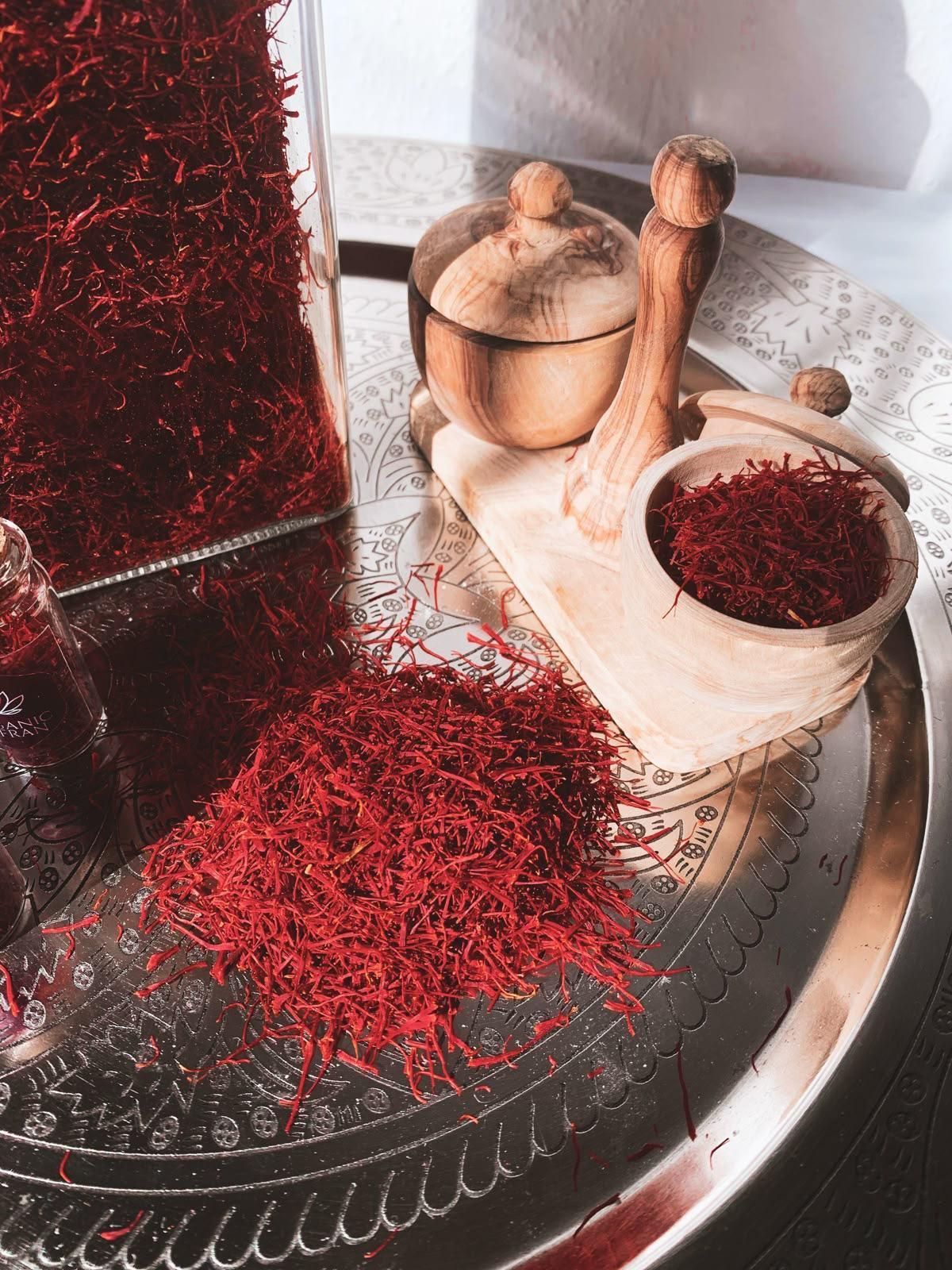 Eine Metalldose, ein Löffel und ein kleines Fläschchen gefüllt mit leuchtend roten Safranfäden vor einem dunkelblauen Hintergrund.