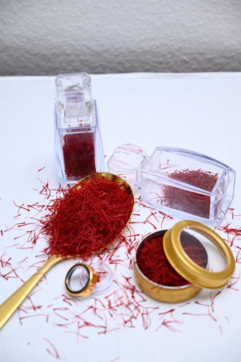 Ein goldener Löffel, bedeckt mit purpurroten Safranfäden, umgeben von Glas- und Metallbehältern, die ebenfalls mit Safran gefüllt sind.