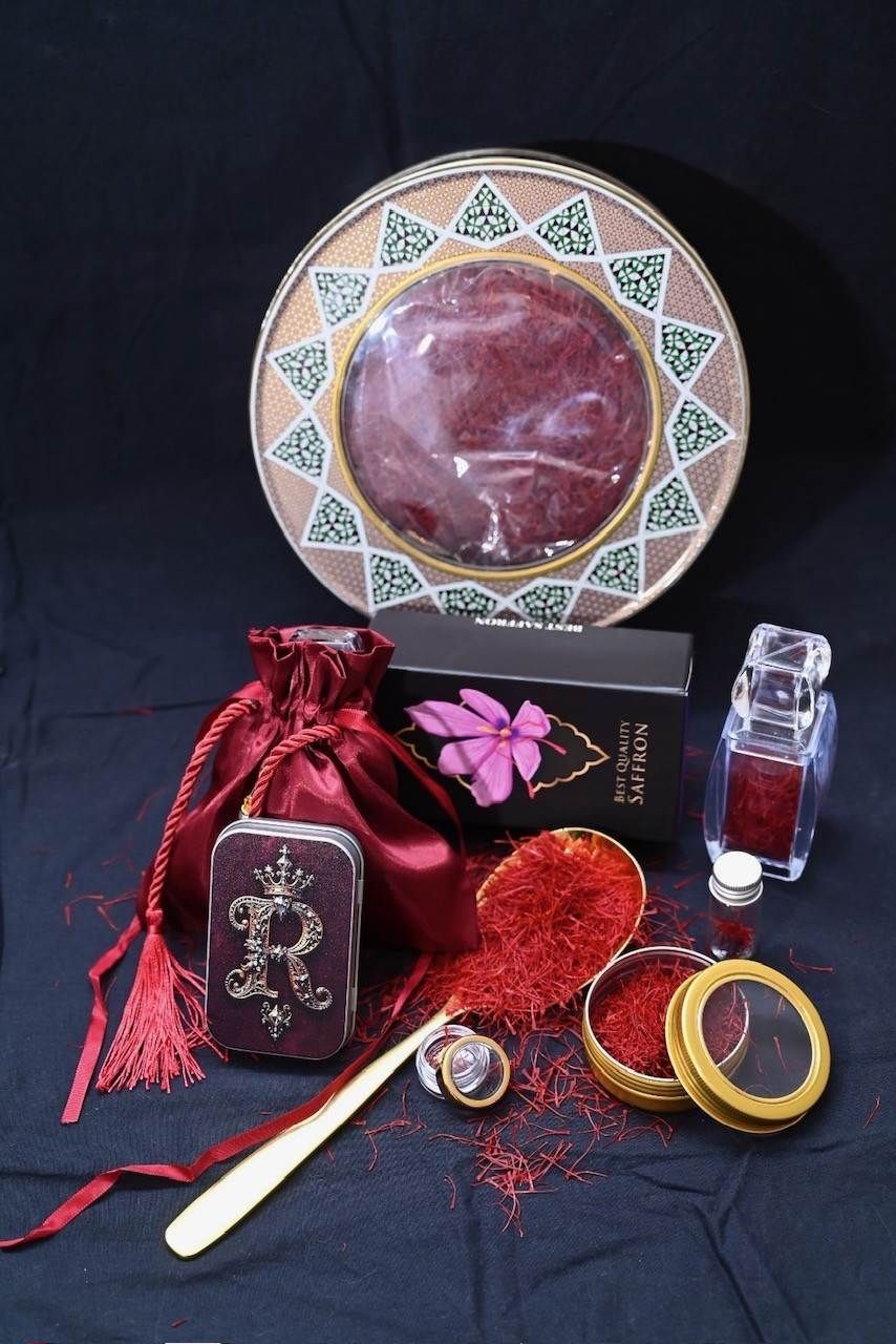Eine Präsentation von Safranprodukten, darunter Dosen, ein Samtbeutel und eine Glasflasche, arrangiert vor dunklem Hintergrund.