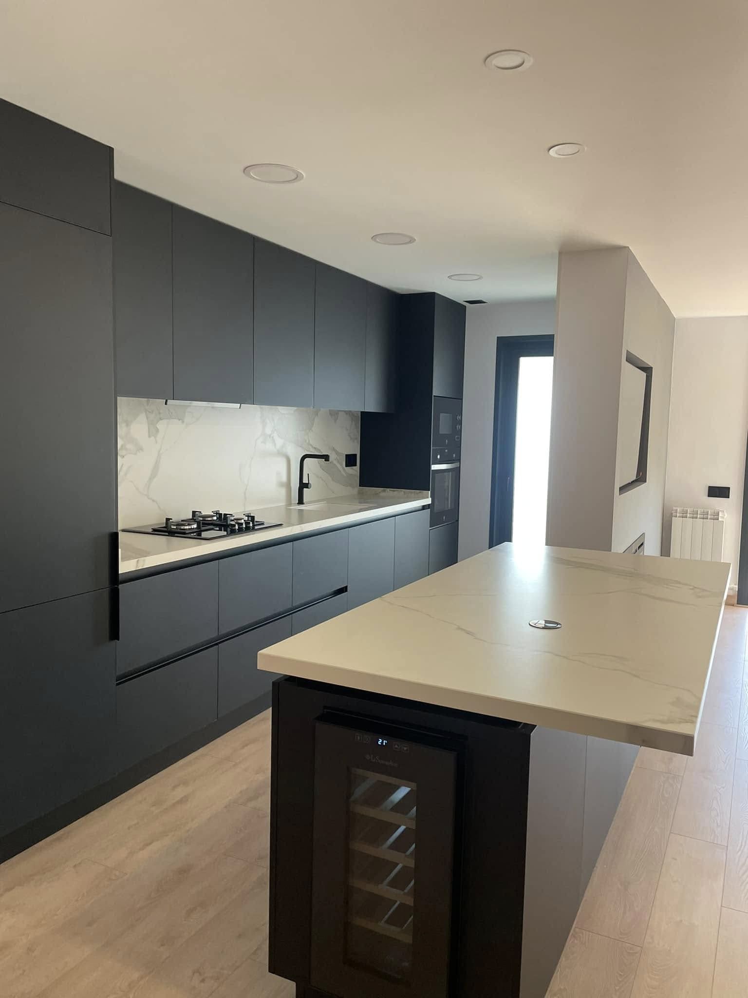 Cocina moderna y minimalista con armarios negros, salpicadero de mármol y una gran isla con nevera para vinos.