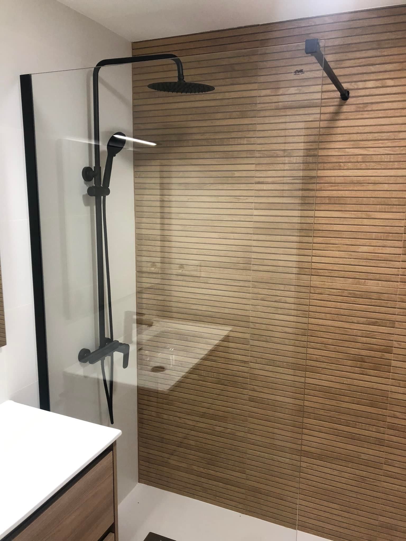 Ducha de baño moderna con mampara de cristal, grifería negra y azulejos de pared texturizados de color beige.