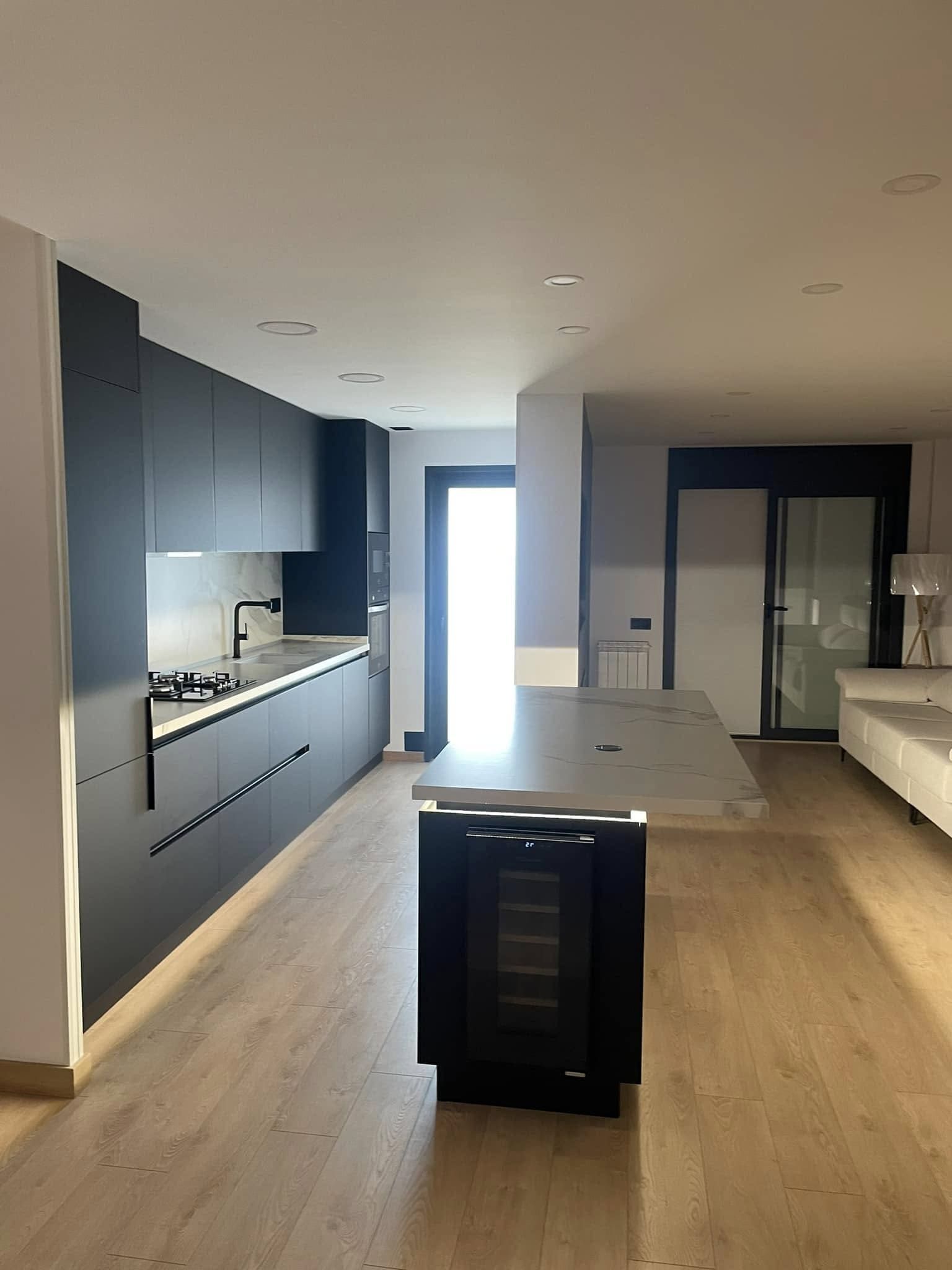 Cocina moderna con gabinetes oscuros, isla, pisos de madera y puertas de vidrio brillante.