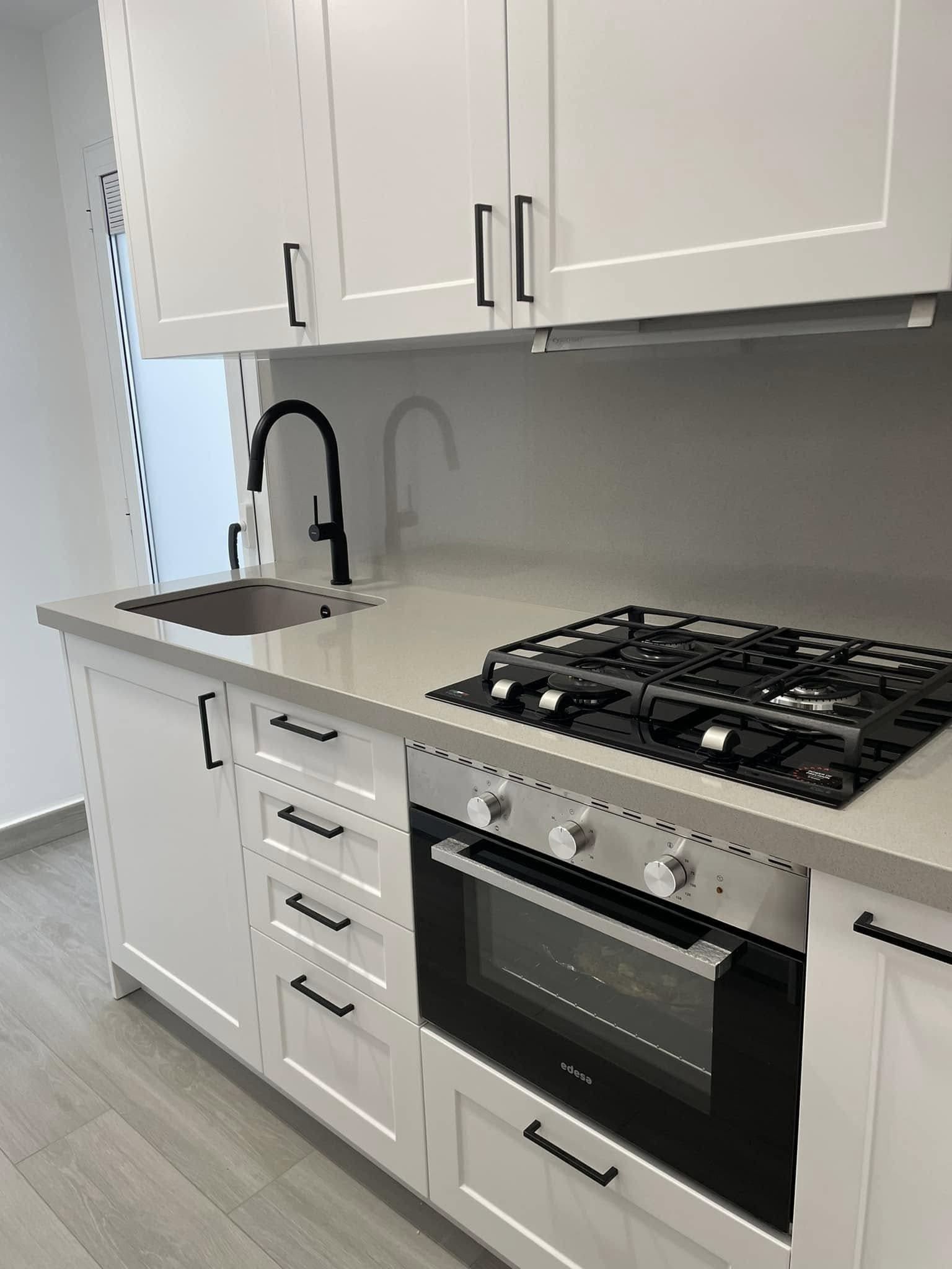 Cocina moderna blanca con grifo negro, salpicadero gris y cocina y horno de acero inoxidable.