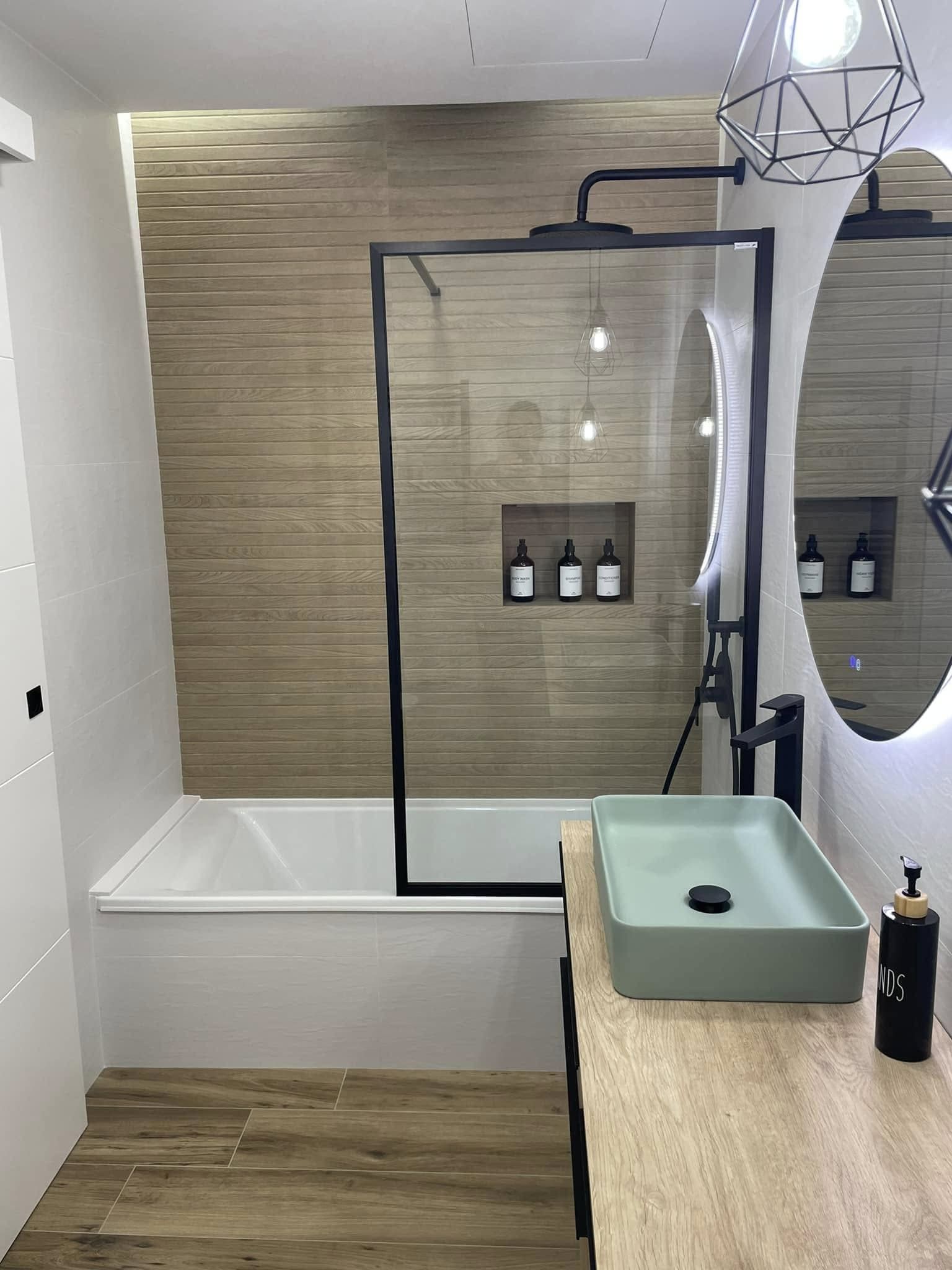 Baño moderno con ducha de cristal, bañera independiente, tocador de madera y detalles de azulejos color menta en el lavabo.