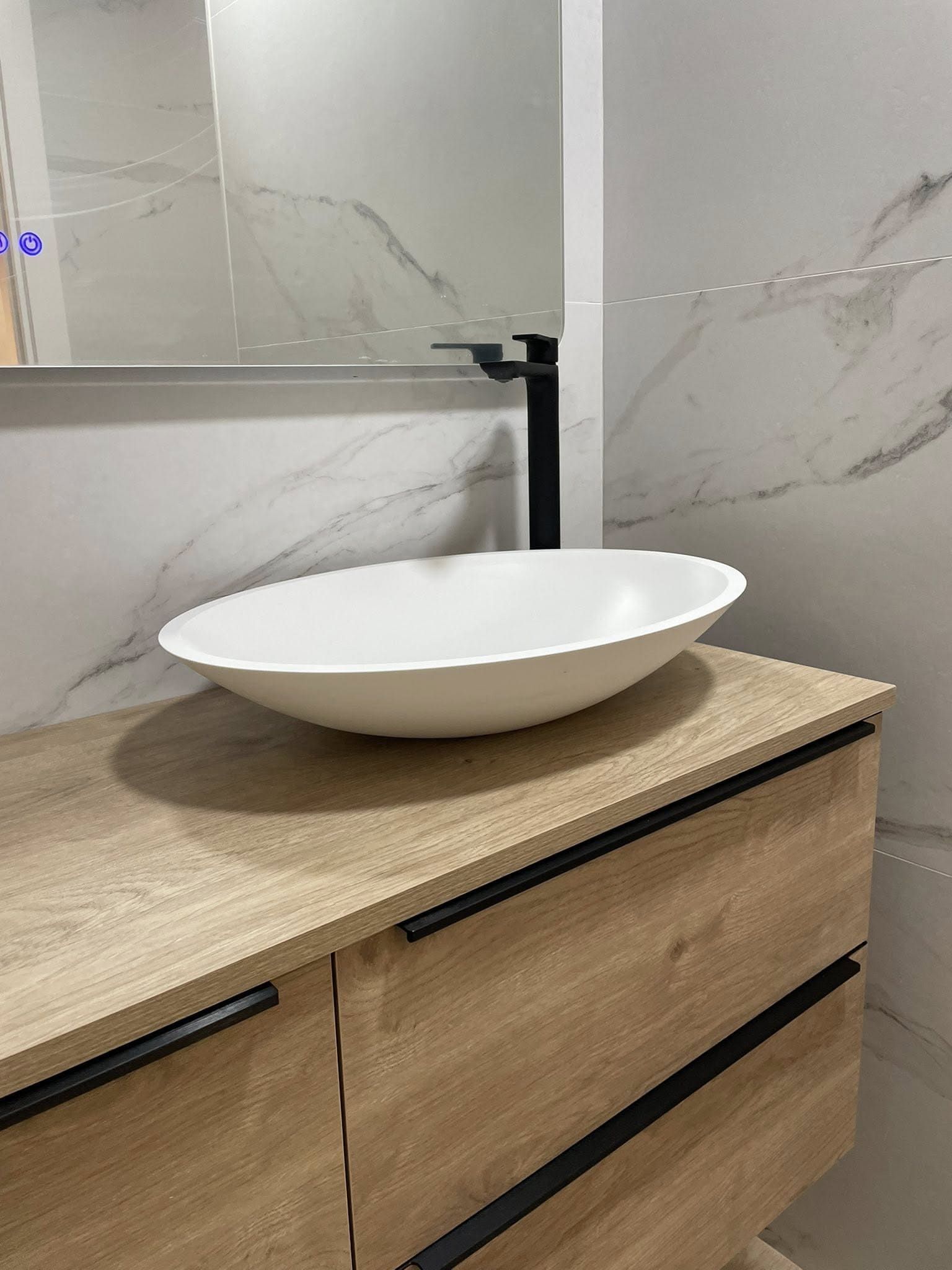 Lavabo ovalado blanco sobre un mueble de madera en un baño moderno.
