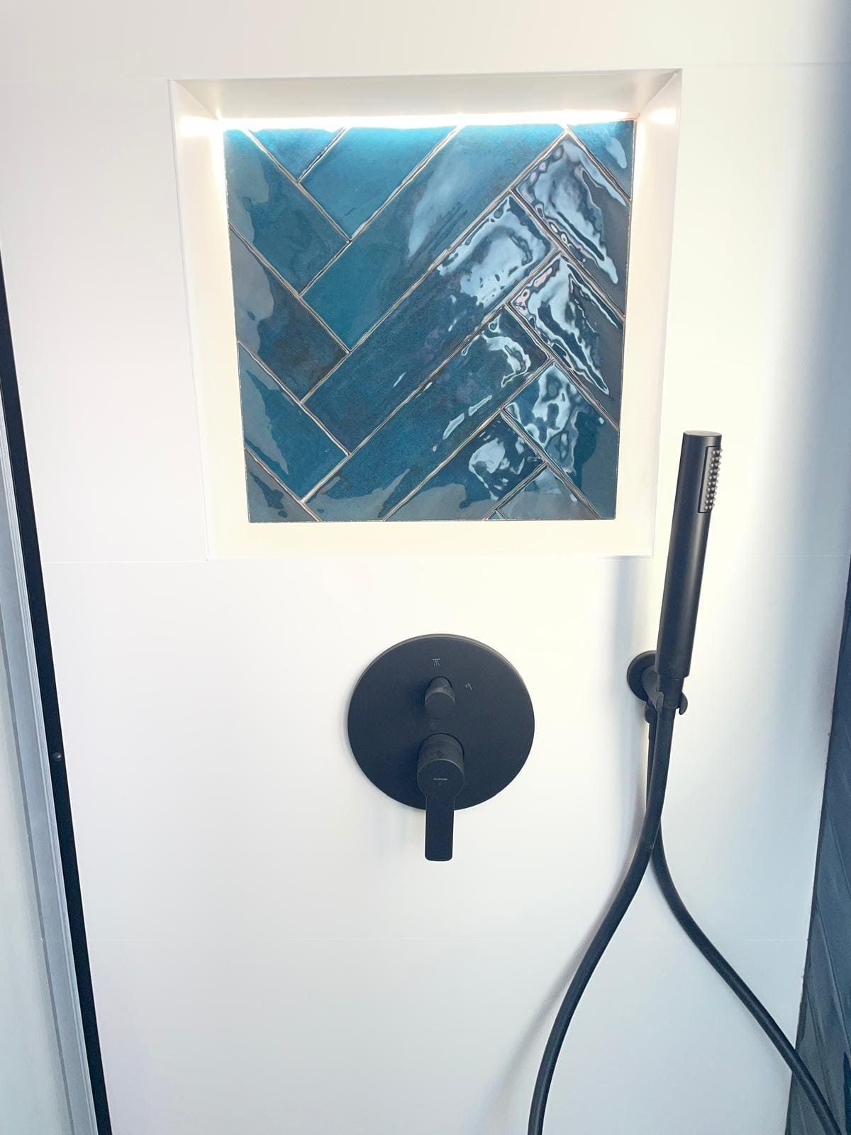 Pared blanca con un cuadro abstracto azul, una lámpara redonda negra y un tubo o soporte negro.