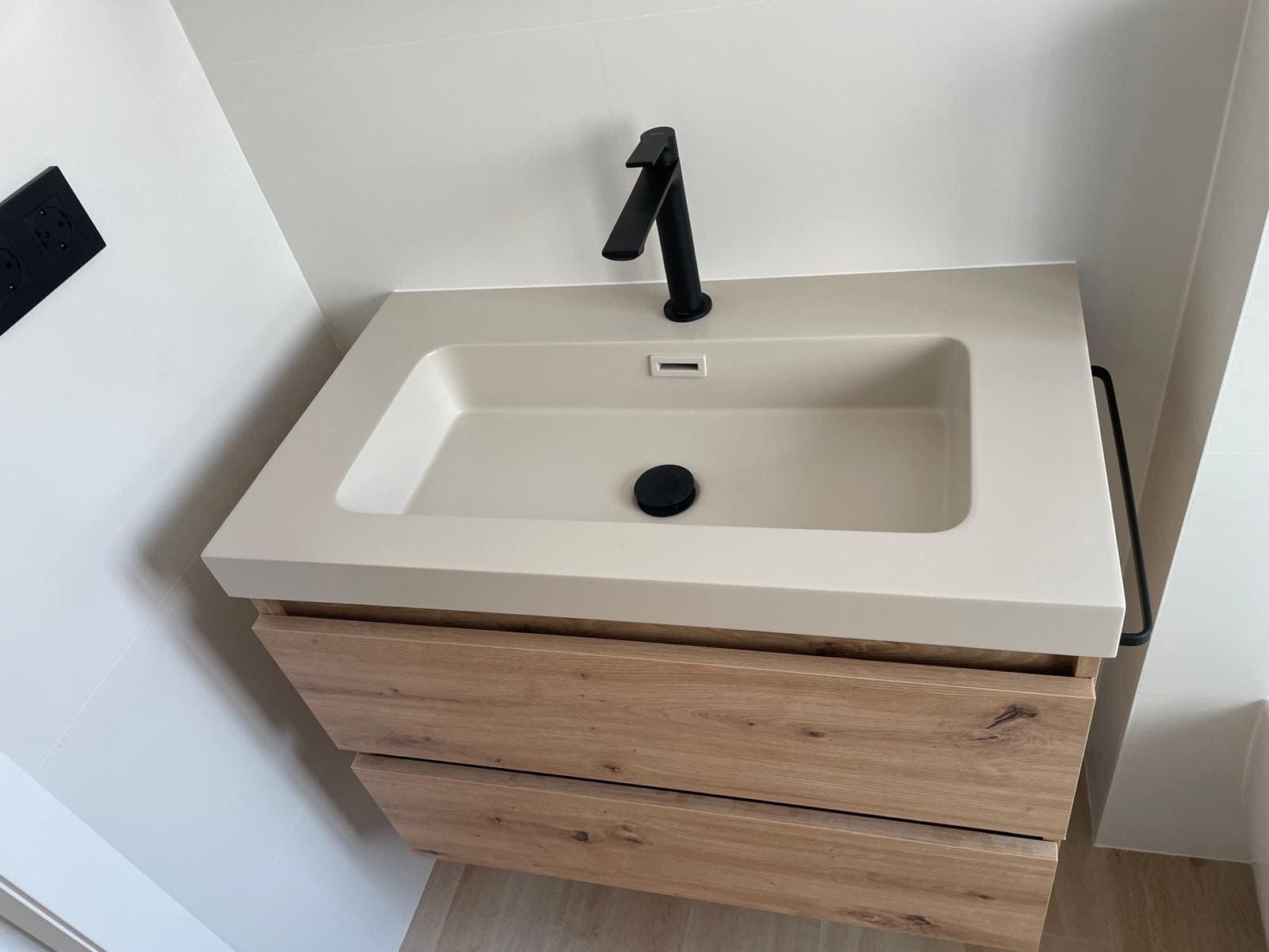 Lavabo de baño moderno de color beige con grifo negro y tocador de madera contra una pared blanca.