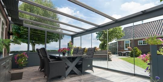Eine Terrasse mit Tisch und Stühlen unter einem Glasdach.