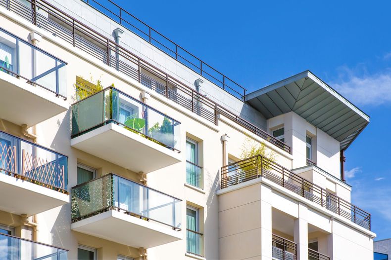 Immeuble d'appartements blanc avec balcons, balustrades en verre et ciel bleu.