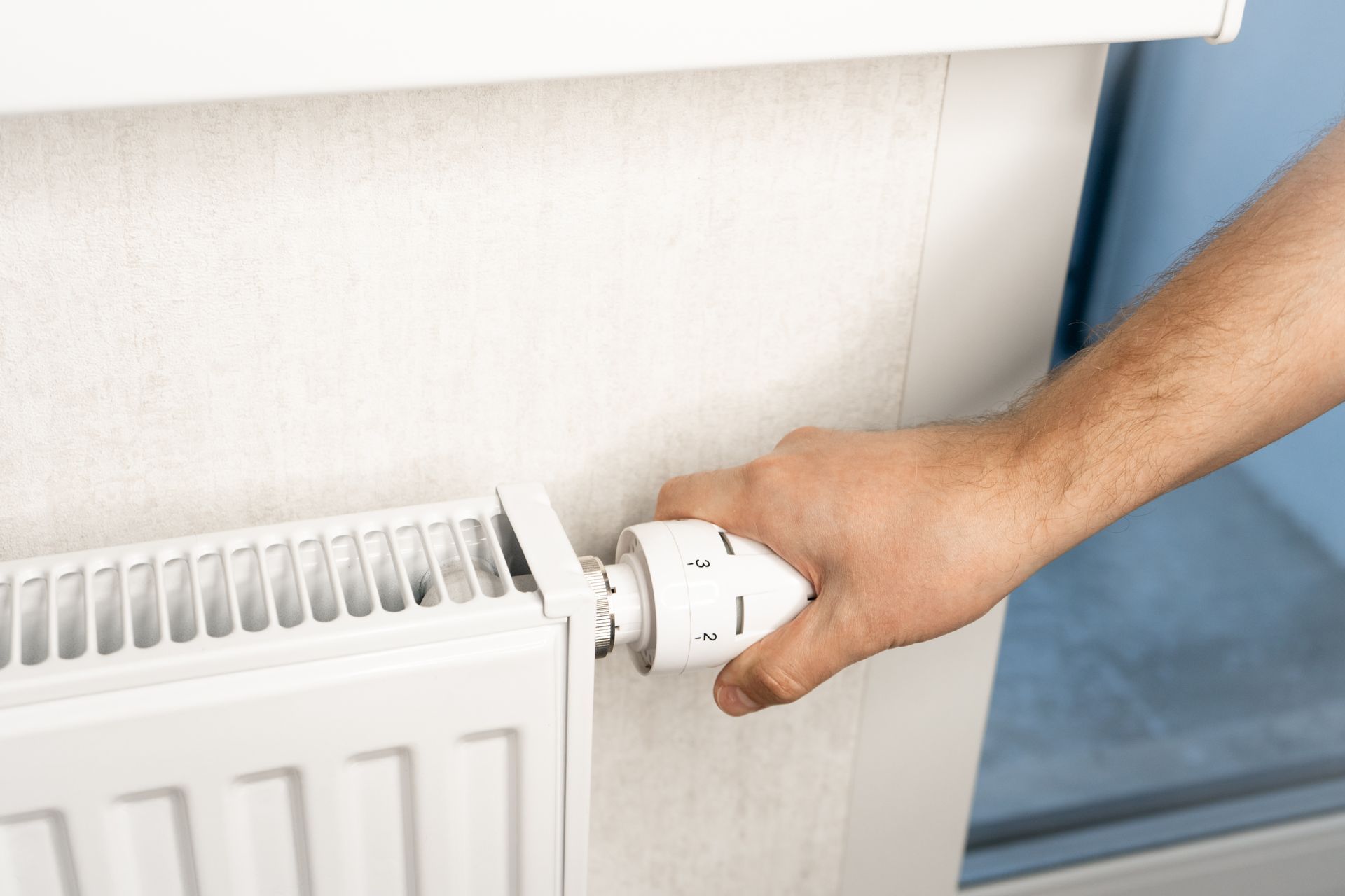 Une main tourne le bouton d'un radiateur blanc.