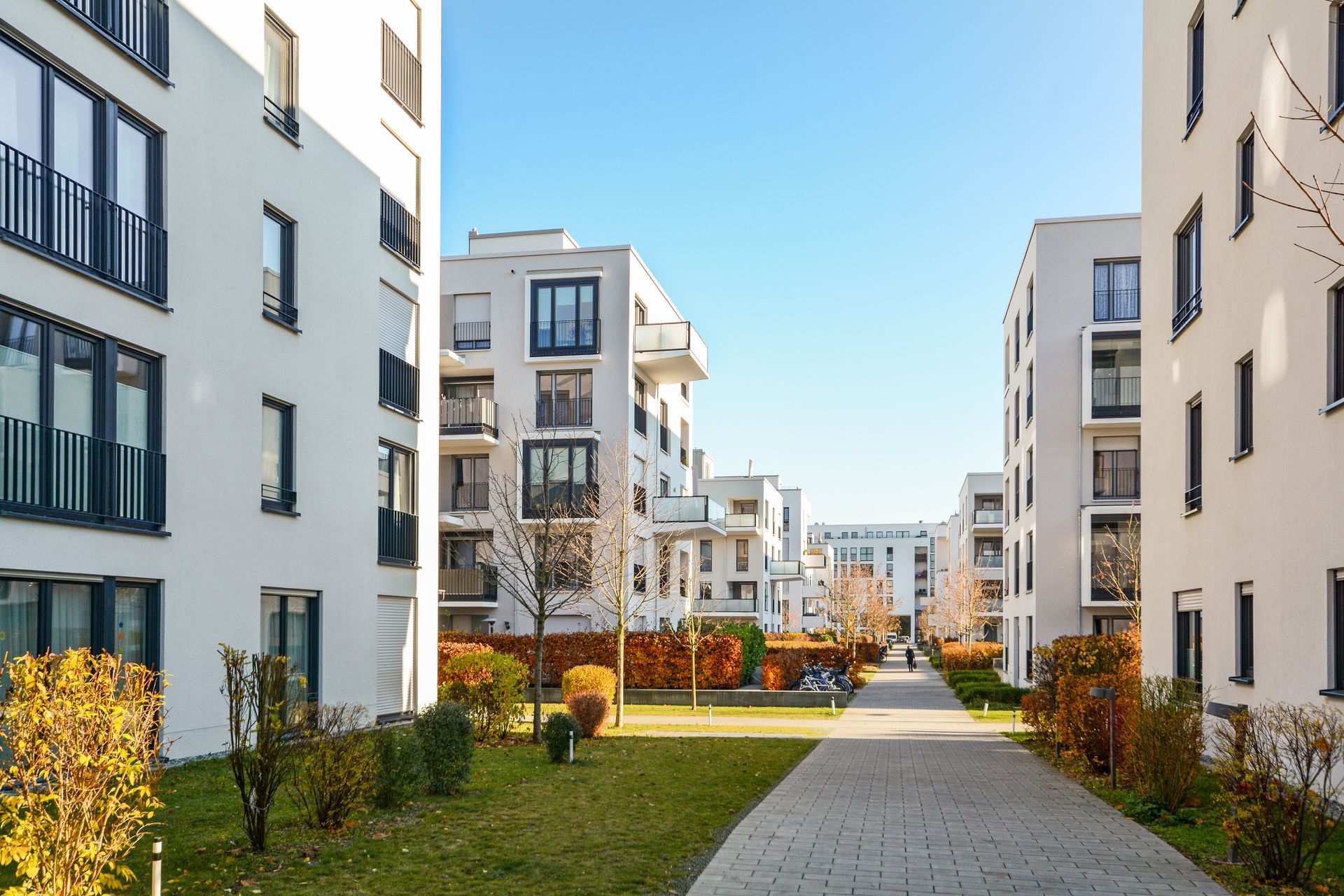 Immeubles d'appartements blancs avec balcons et allées, espaces verts, ciel bleu azur.