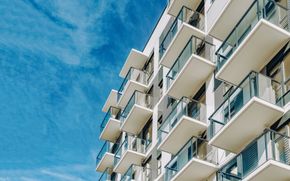 Immeuble d'appartements blanc avec balcons se détachant sur un ciel bleu clair nuageux.