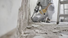 Une personne utilise un marteau-piqueur pour enlever du plâtre d'un mur dans une pièce.