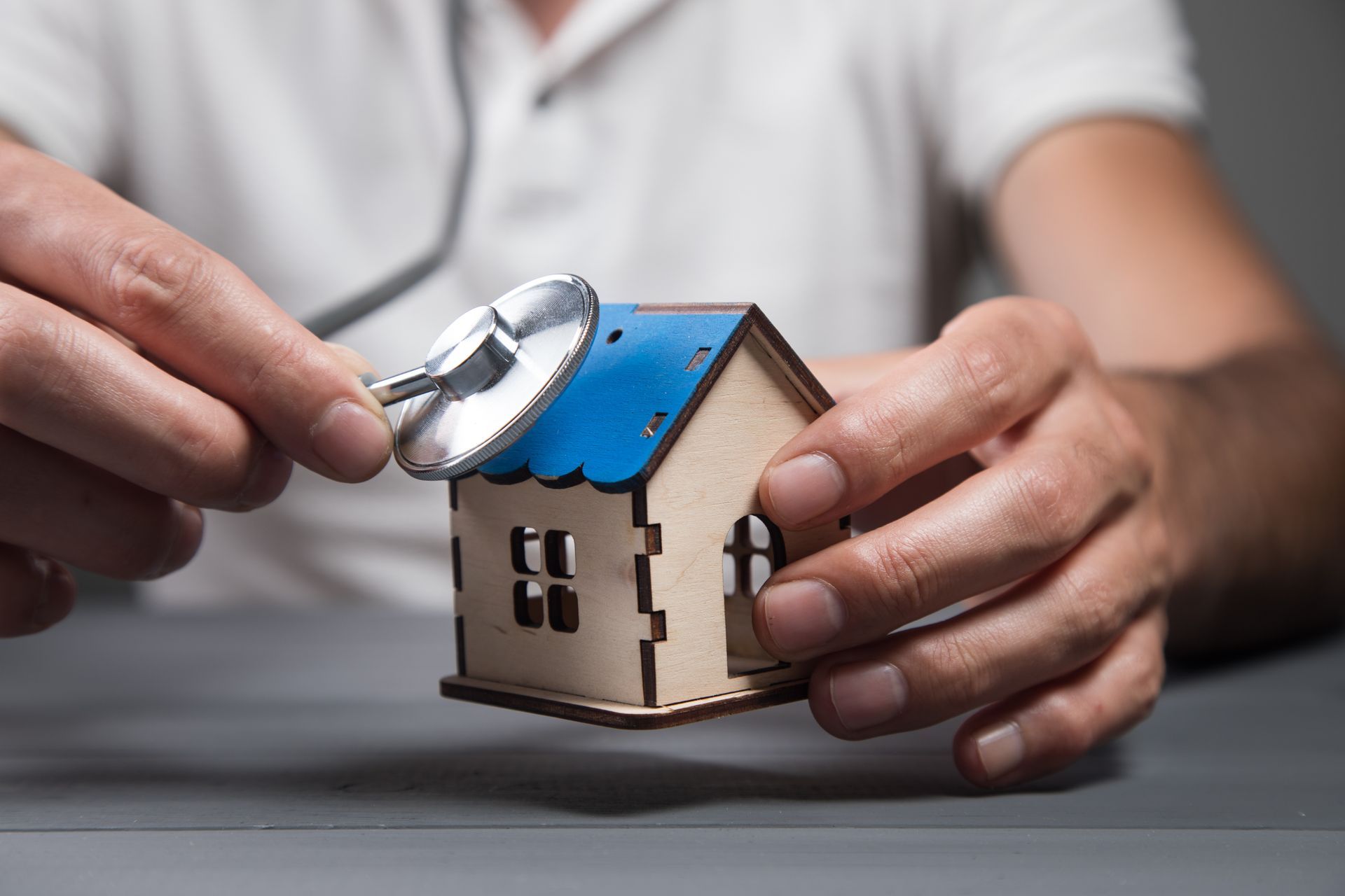 Une personne tenant un stéthoscope devant une maison miniature.