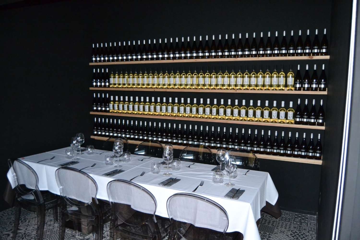 Un comedor con una mesa y sillas frente a una pared de botellas de vino.