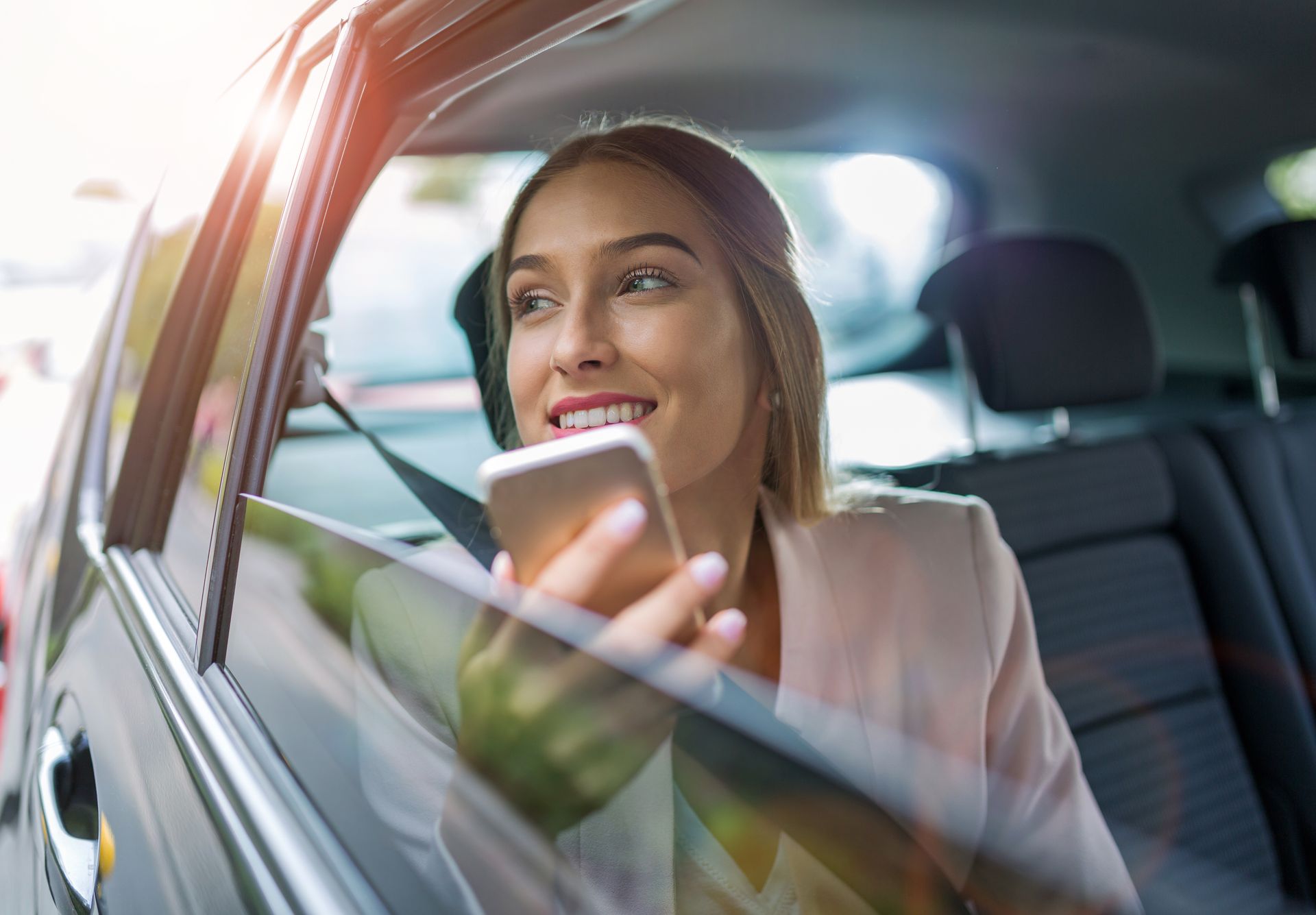 Femme en voiture, regardant par la fenêtre tout en tenant son téléphone.