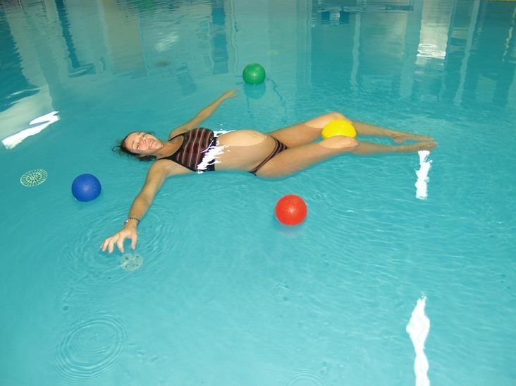 Mujer embarazada flota en una piscina con pelotas de ejercicio, sonriendo.