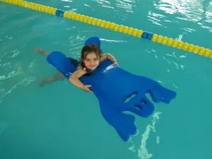 Una niña sonríe mientras flota en un flotador de espuma azul en una piscina.