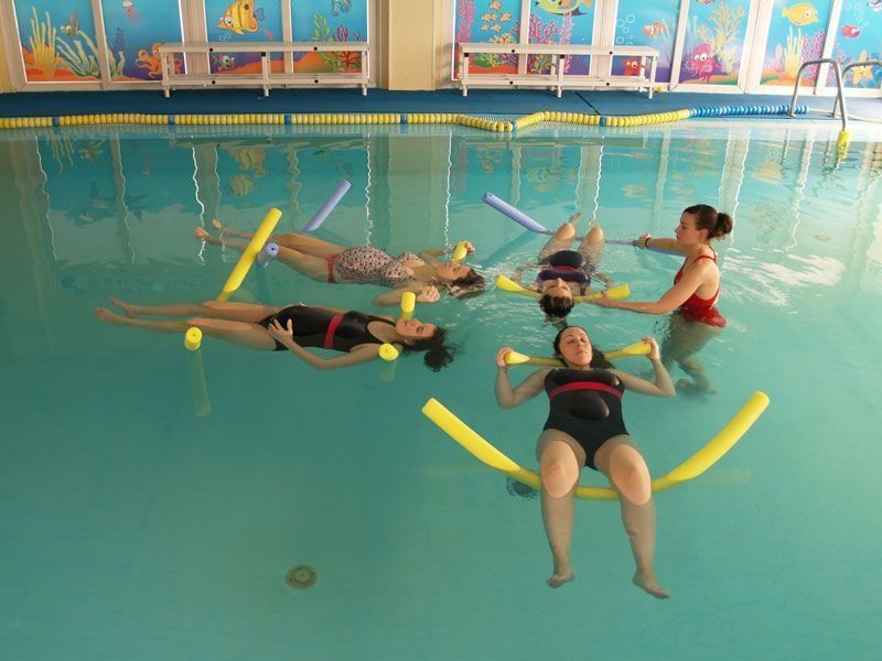 Mujeres en una piscina usando dispositivos de flotación con un instructor, probablemente para terapia acuática.
