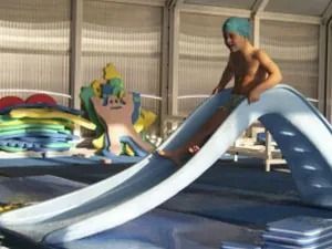 Niño con gorro de baño azul deslizándose por un tobogán de piscina. Piscina cubierta.
