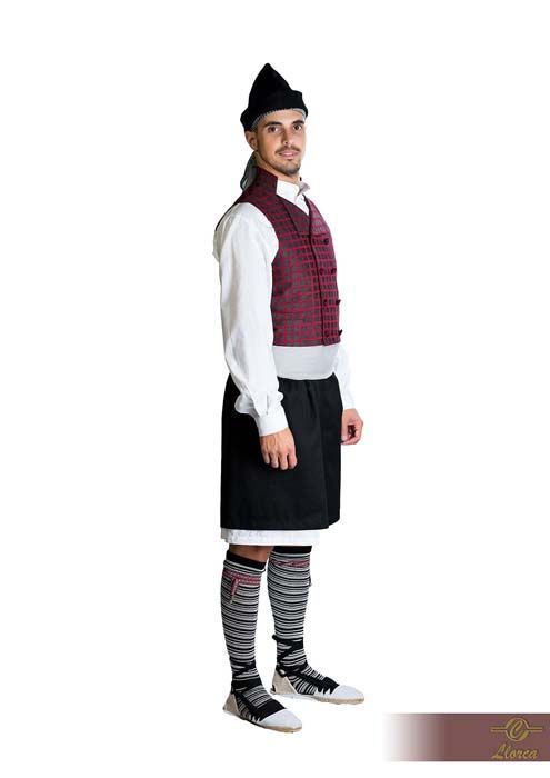 Una persona de pie sobre un fondo blanco, vestida con un atuendo tradicional compuesto por un chaleco granate, una falda escocesa negra y calcetines a rayas.