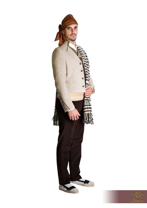 Una persona vestida con un traje folclórico tradicional español: una chaqueta color canela, pantalones marrones, pañuelo en la cabeza y un chal a rayas sobre los hombros.