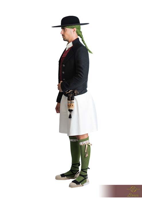 Una persona con atuendo folclórico tradicional que incluye sombrero negro, chaqueta oscura, falda blanca, medias verdes y zapatos con cordones.