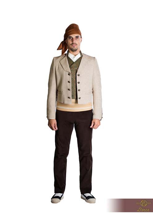 Una persona con atuendo folclórico tradicional español: pañuelo marrón en la cabeza, chaqueta beige, chaleco verde, pantalones oscuros y zapatillas de lona.