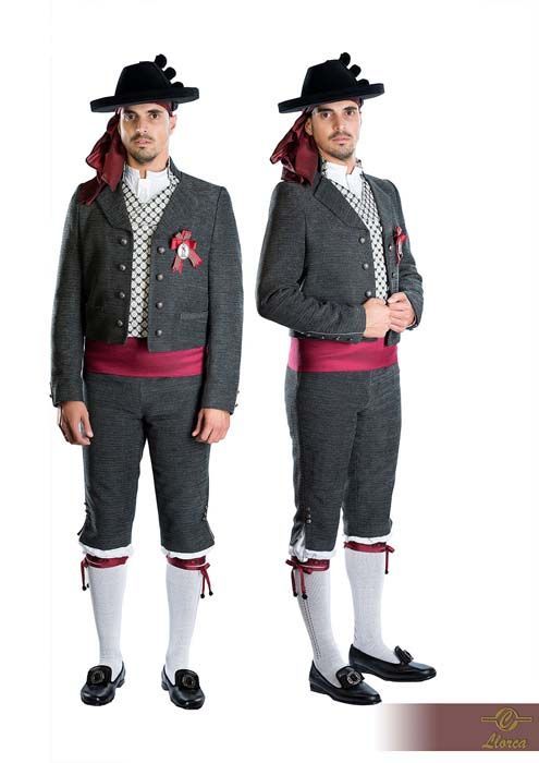 Dos personas vestidas con trajes folclóricos tradicionales españoles, que consisten en trajes grises, fajas rojas, sombreros y medias blancas.