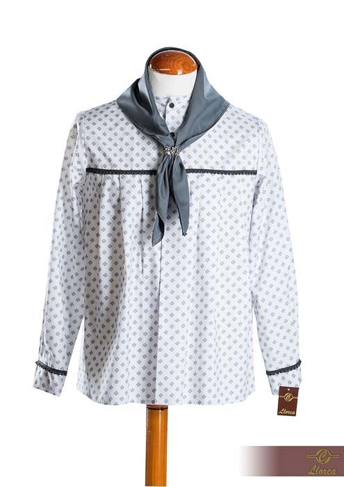 Una camisa blanca de manga larga con un pequeño estampado floral azul, ribete azul oscuro y una bufanda a juego en el cuello, exhibida en un maniquí.