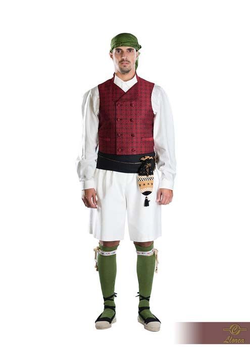 Una persona vestida con una camisa blanca, un chaleco rojo estampado, pantalones cortos blancos, calcetines verdes y un pañuelo verde en la cabeza, sobre un fondo blanco.