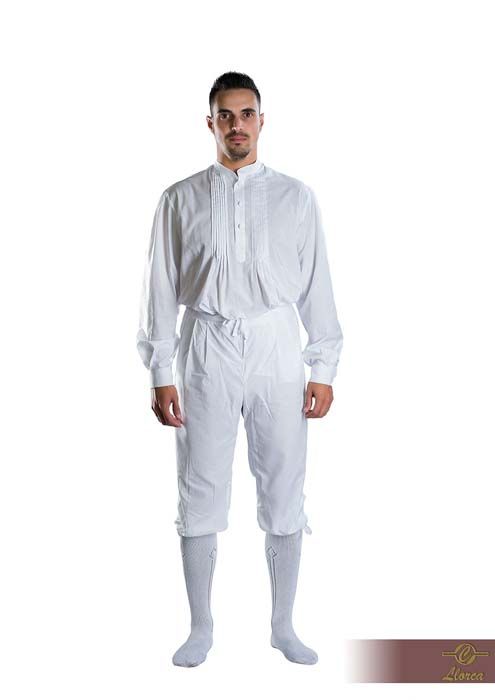 Una persona vestida con una camisa blanca de estilo histórico, pantalones hasta la rodilla y calcetines hasta la rodilla, sobre un fondo blanco.