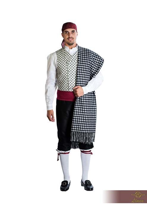 Una persona vestida con atuendo folclórico tradicional que incluye un chaleco estampado, pantalones oscuros, un chal a cuadros y un pañuelo rojo en la cabeza.