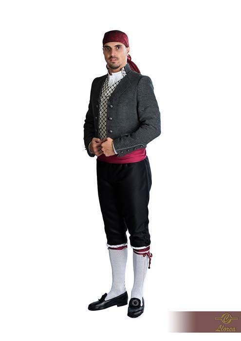 Un hombre que viste un traje tradicional compuesto por una chaqueta oscura, un chaleco a cuadros, pantalones negros y un pañuelo granate en la cabeza.